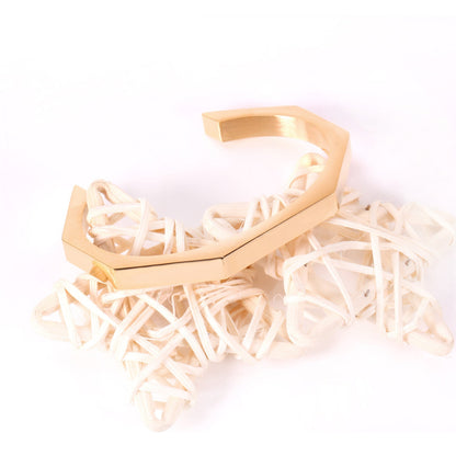 Gold-tone steel with an angular face on an open-end rigid bracelet.